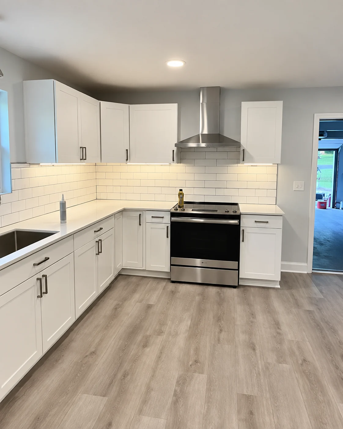 White kitchen with stainless steel appliances and gray wood flooring from Elite’s renovation reel