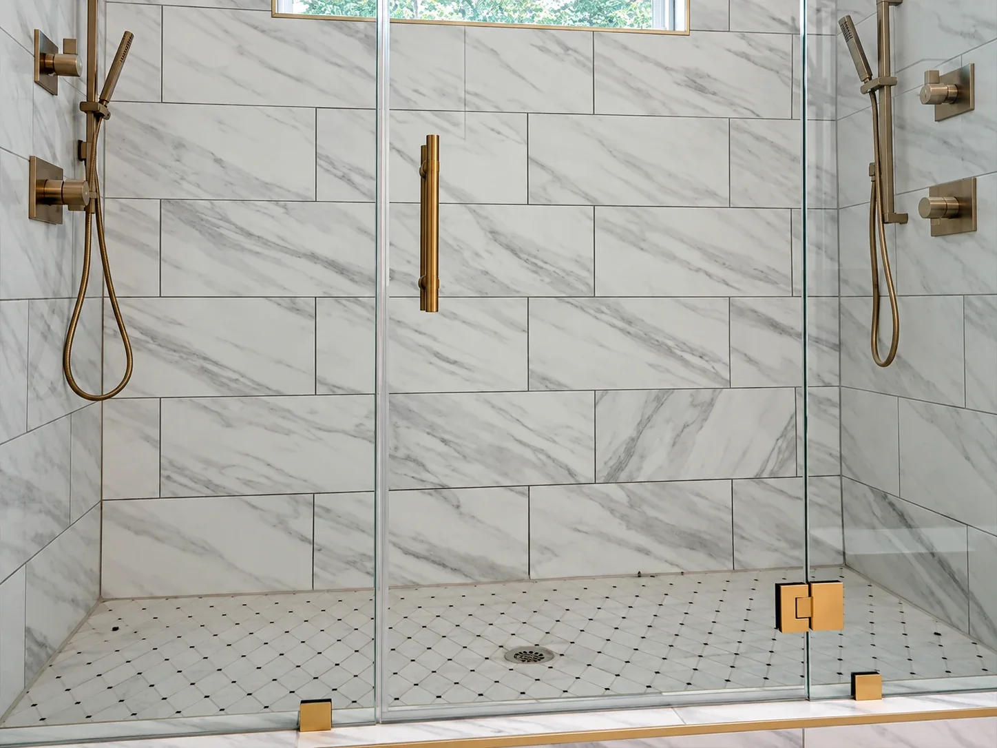 Marble-look walk-in shower with glass door and brass fixtures, enhanced from Elite’s Instagram