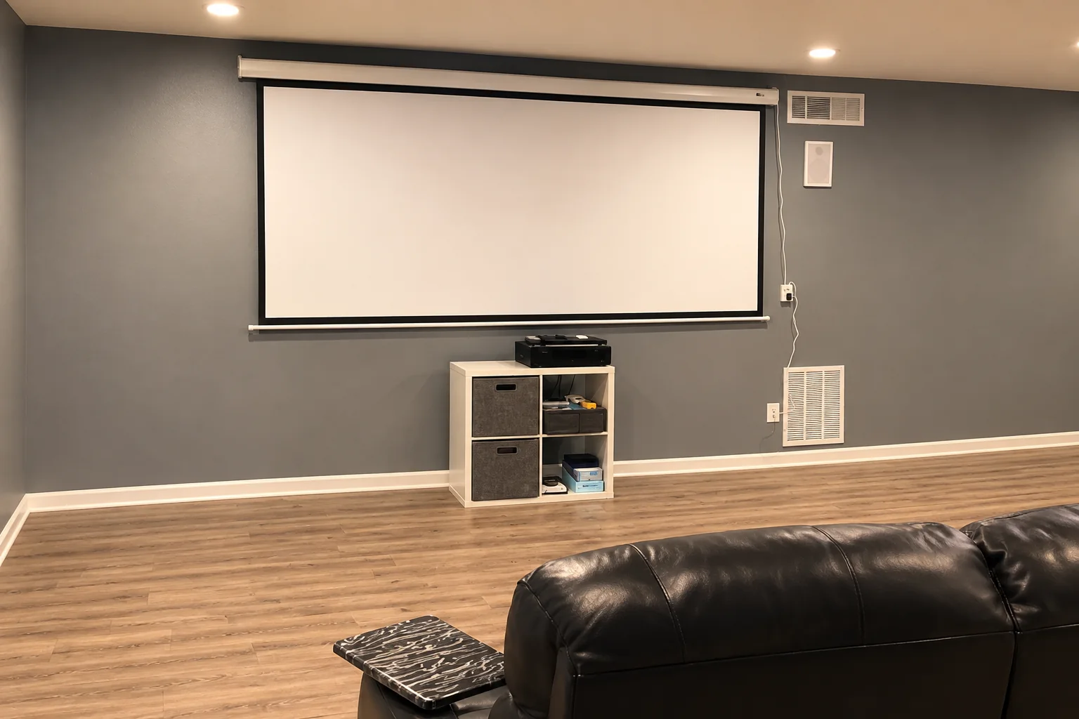 Gray media room with wood floors and a black sofa, AI-enhanced from Elite’s Instagram